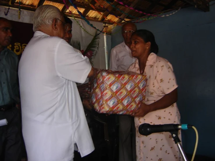 a group of people standing in front of a woman who is presenting a gift