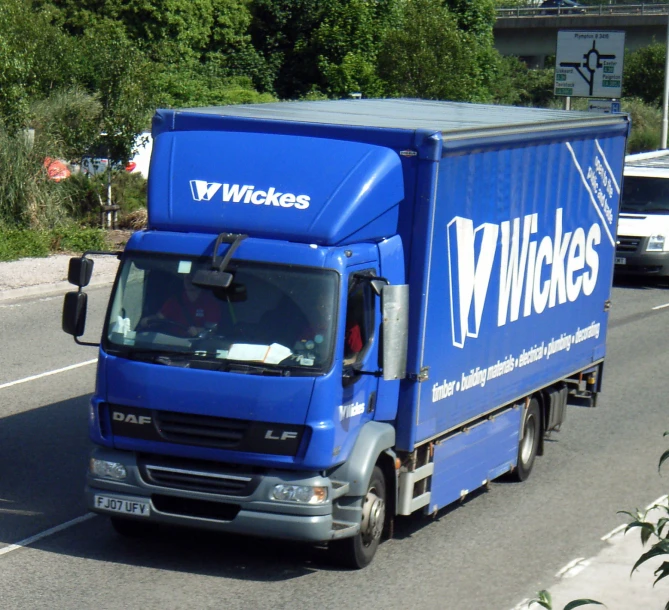 the blue truck drives on the road next to the forest