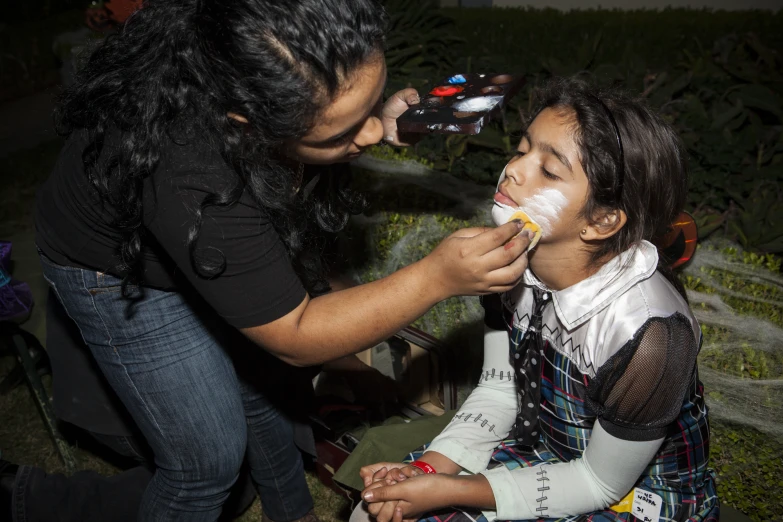 two women are putting white powder on one of the girls's faces