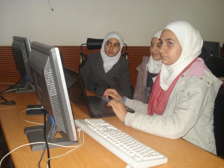 two woman sit on computer with keyboard and monitor next to them