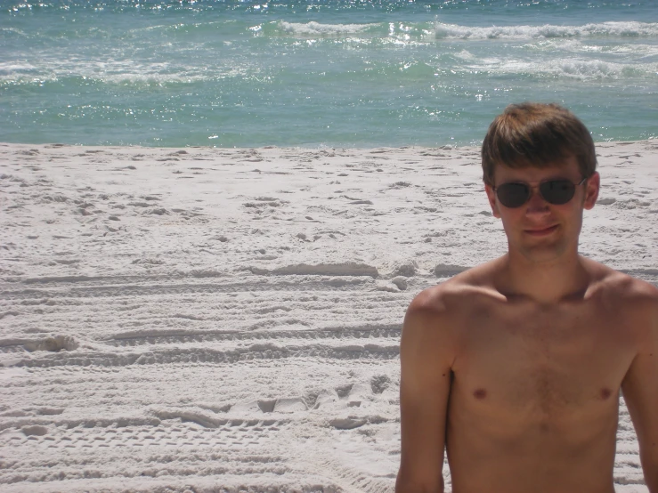 a shirtless man in sunglasses stands on the beach