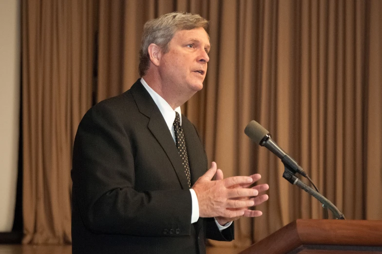 a man with glasses and an tie speaks to the crowd