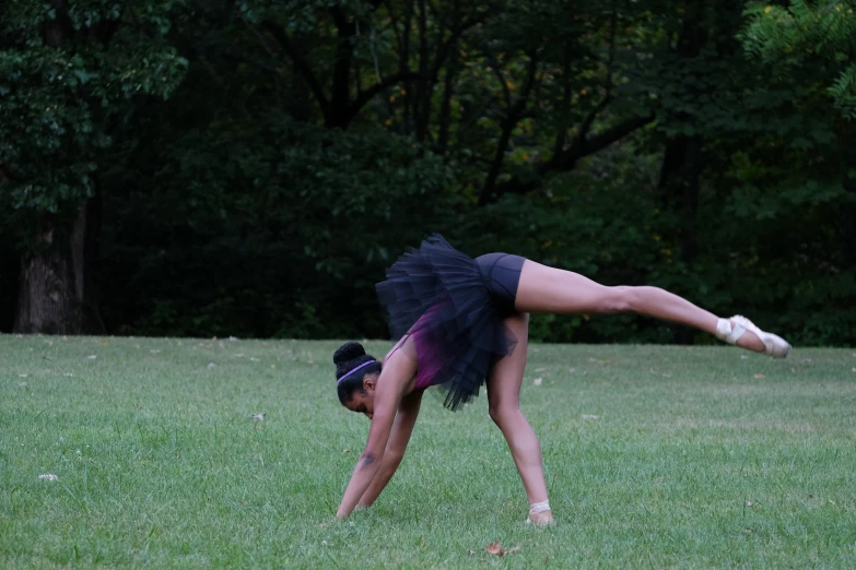 a young woman practicing a ballet pose on the grass