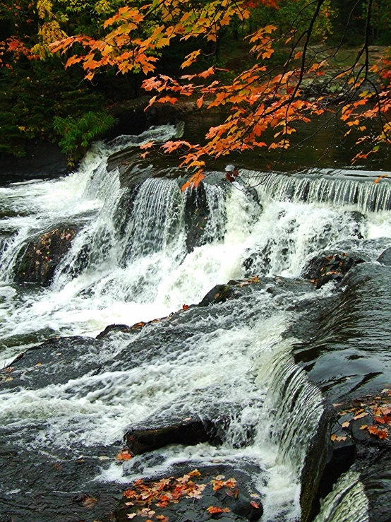 a man is sitting on rocks beside the waterfall