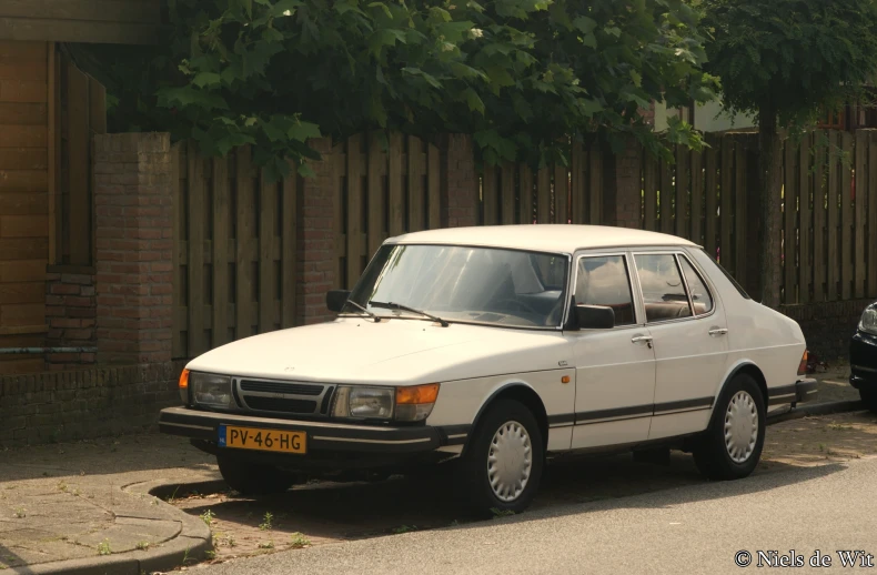 an older white car sits in front of a newer white car