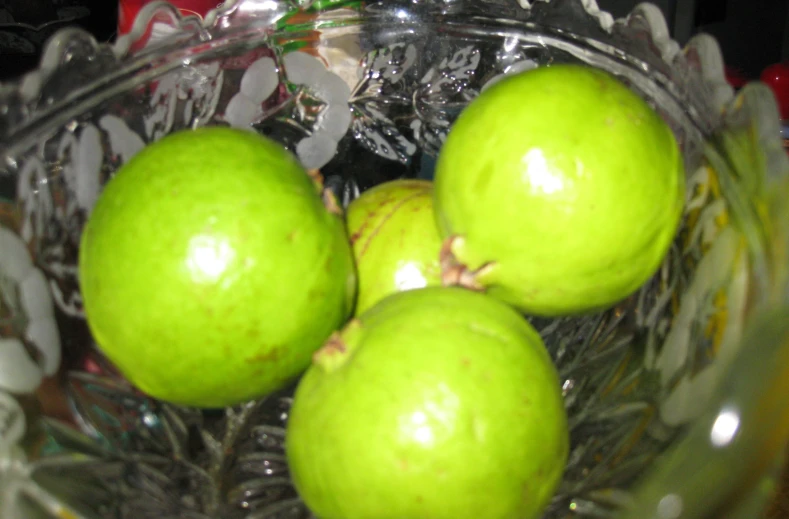 four green apples in a glass bowl next to each other