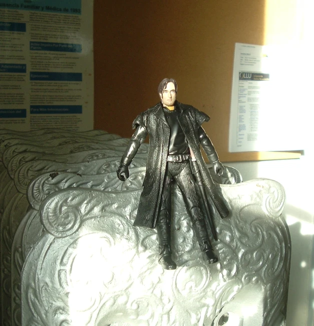 a plastic toy dressed in black is sitting on a sheet