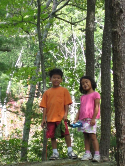two children stand on the log in the woods