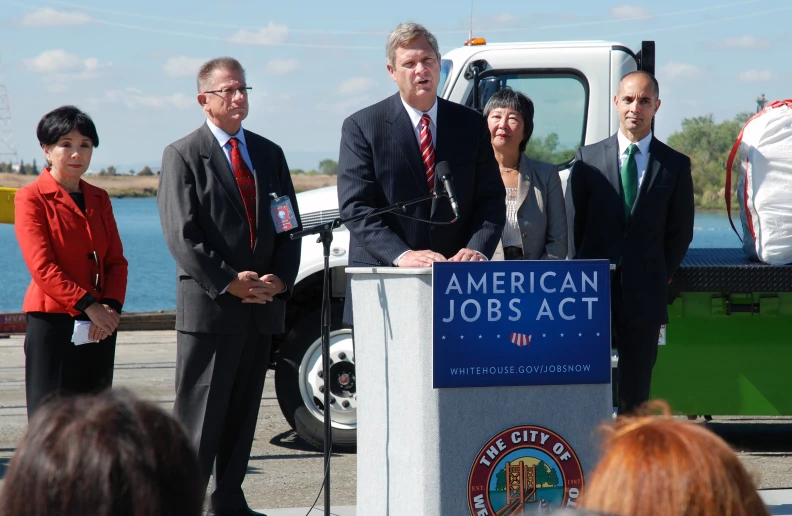 four people standing behind a microphone in front of a truck