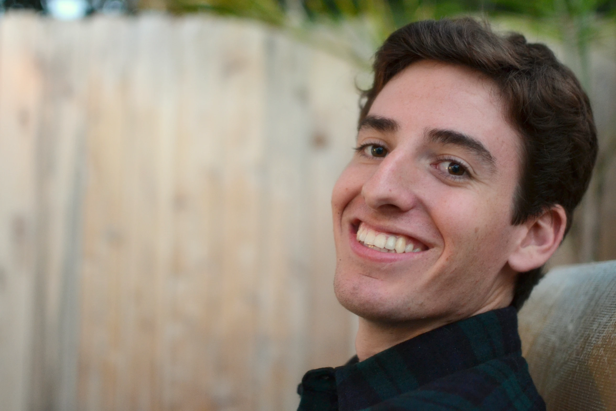 a man smiles with a wood fence behind him