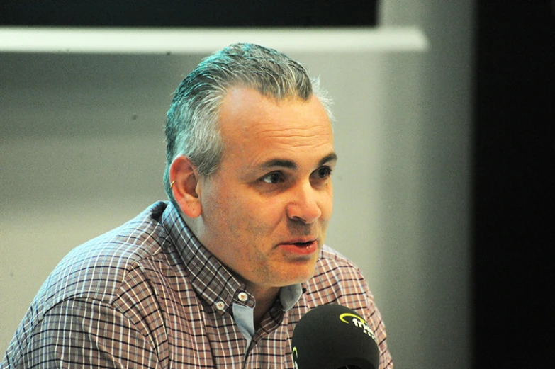 a man with grey hair and no shoes sitting down and talking into a microphone