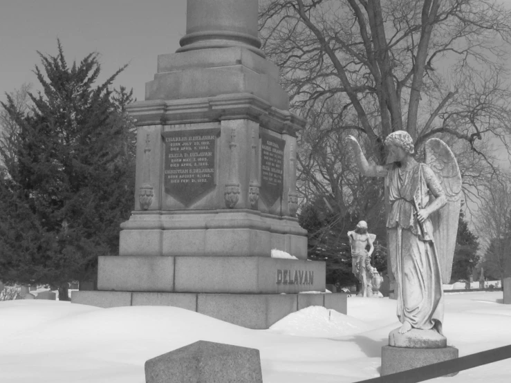 a statue of an angel in the snow by a tree