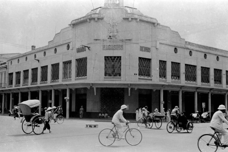 black and white pograph of men riding bikes and carriages in front of an old store