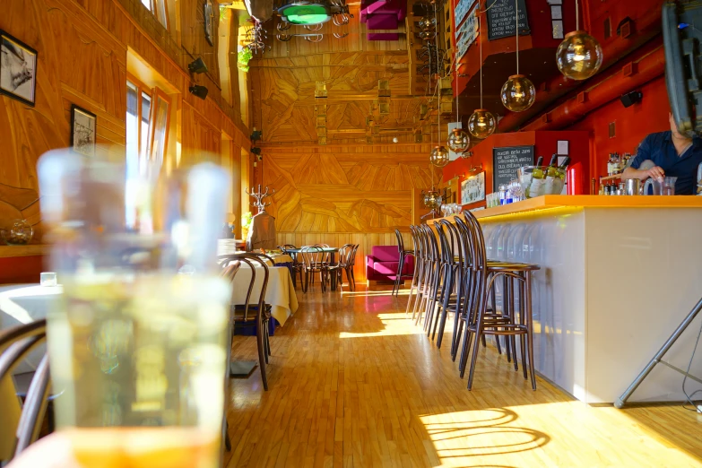 a long narrow restaurant with chairs on the side and a bright orange wall