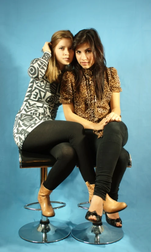 two women sitting down on stools posing for a picture