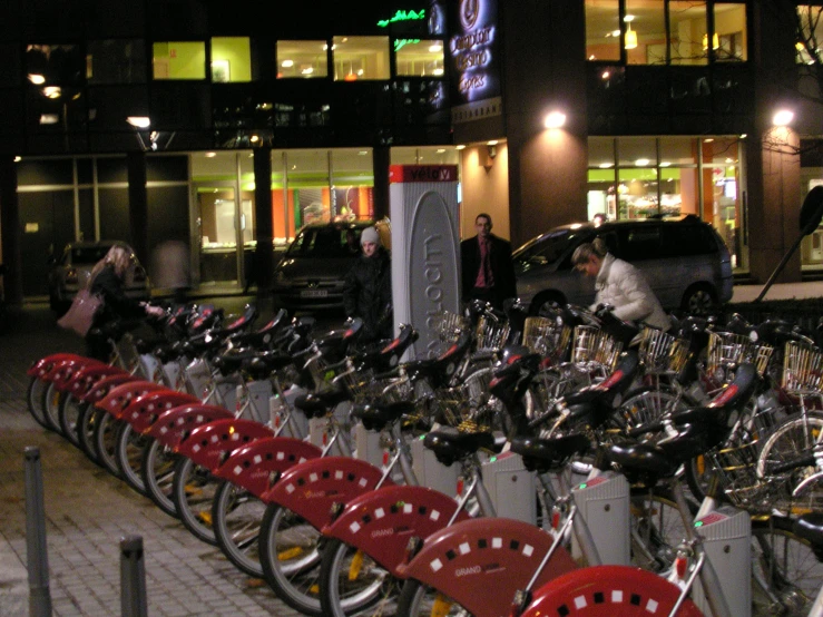 a line of bikes with people walking by on a street at night