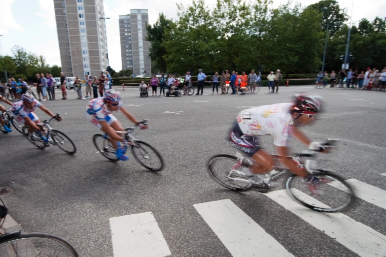 several men racing bicycles down a street with many people standing around