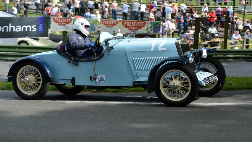 a man in a helmet driving an old blue race car