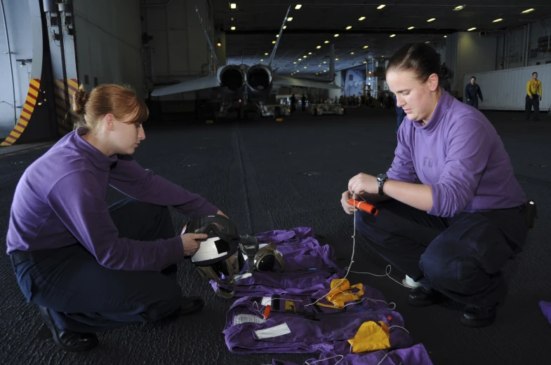 two women in purple shirts working on some small airplanes