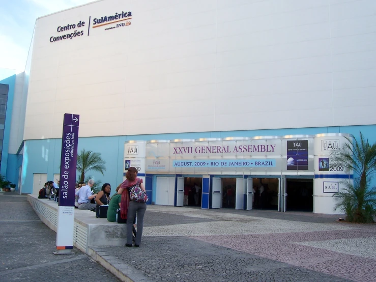 two people walk in front of a building with large banner