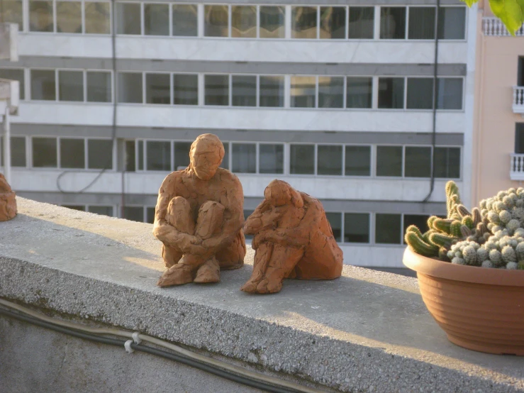 three clay figurines sit on top of a concrete wall near cactuses and buildings