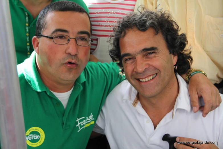 two men are standing side by side wearing green shirts