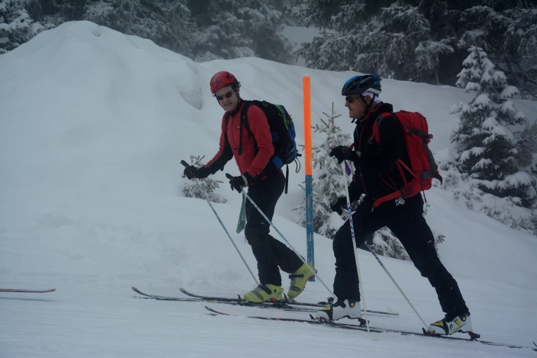 two people on skis with back packs and hats, walking through snow