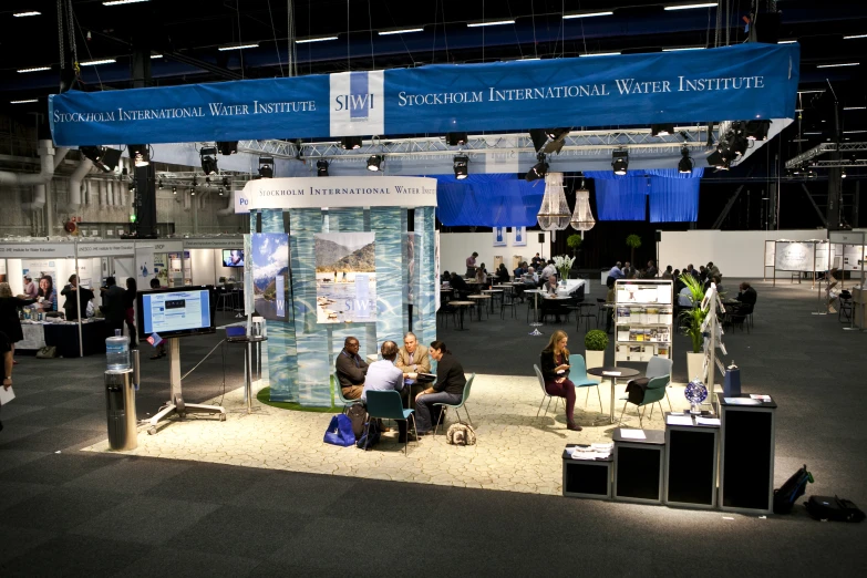 a group of people standing around a booth with people sitting at the table