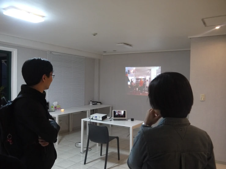 two men standing around and looking at the television