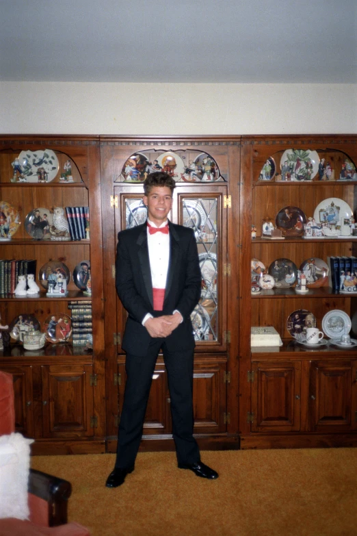 a man in a tuxedo standing in front of some shelves of china