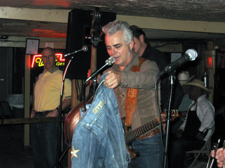 a man in tan jacket holding guitar in front of microphone
