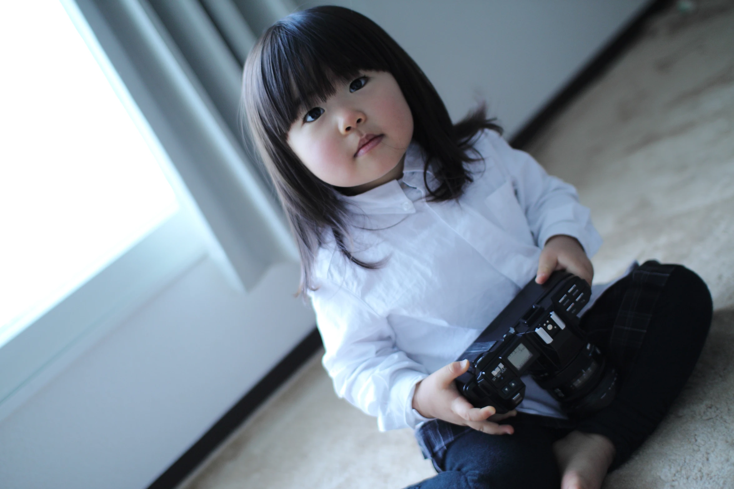 a small girl wearing jeans holding a remote control