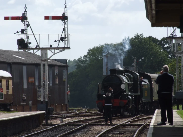 a small train pulling into a station with some people standing on the platform and looking at the train