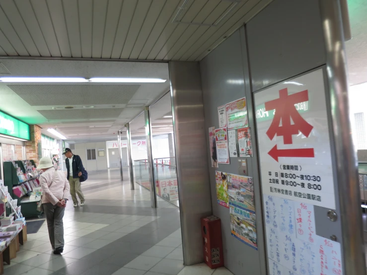 a walkway is seen with a sign and some people walking down the hall