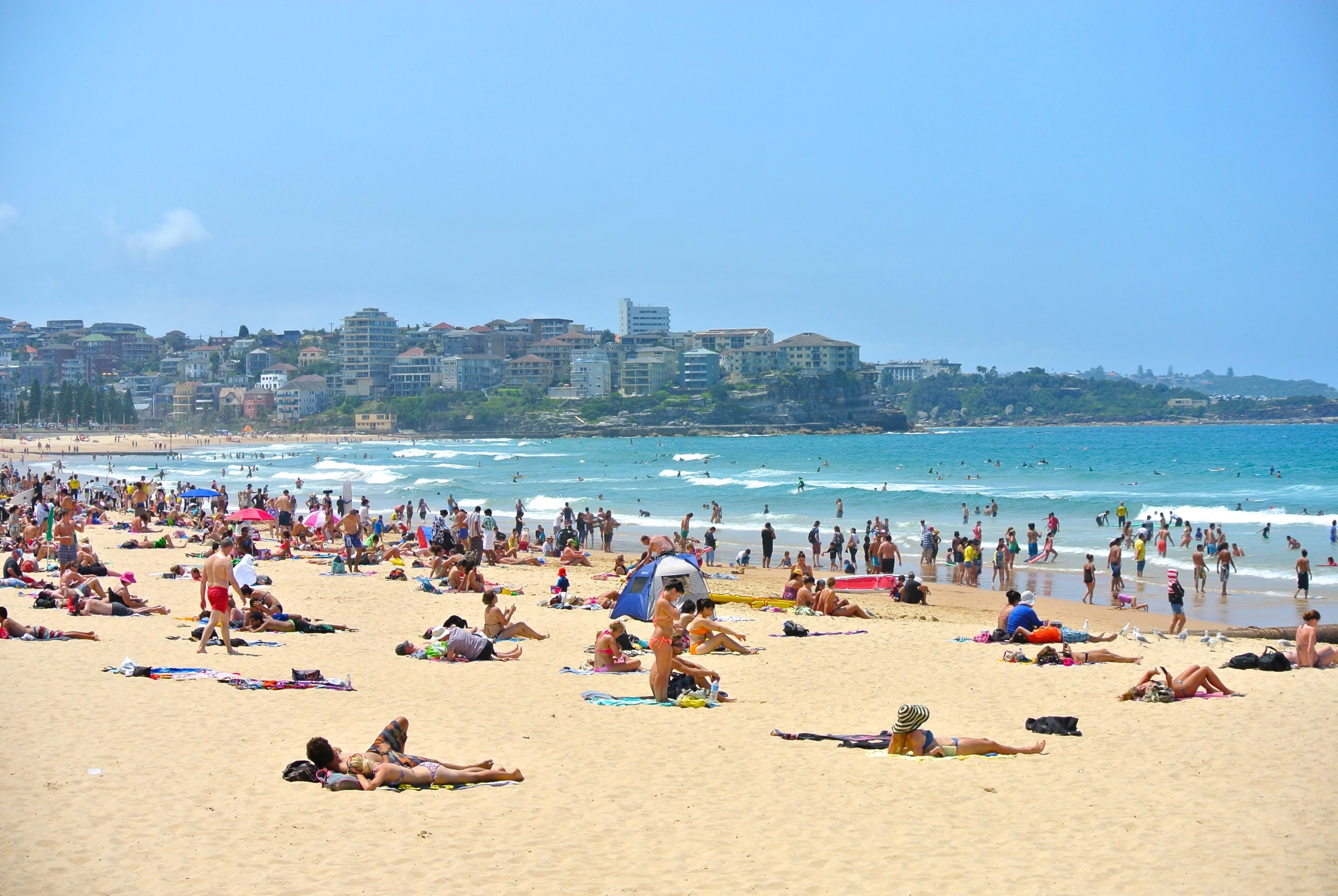 a crowded beach with a city in the background