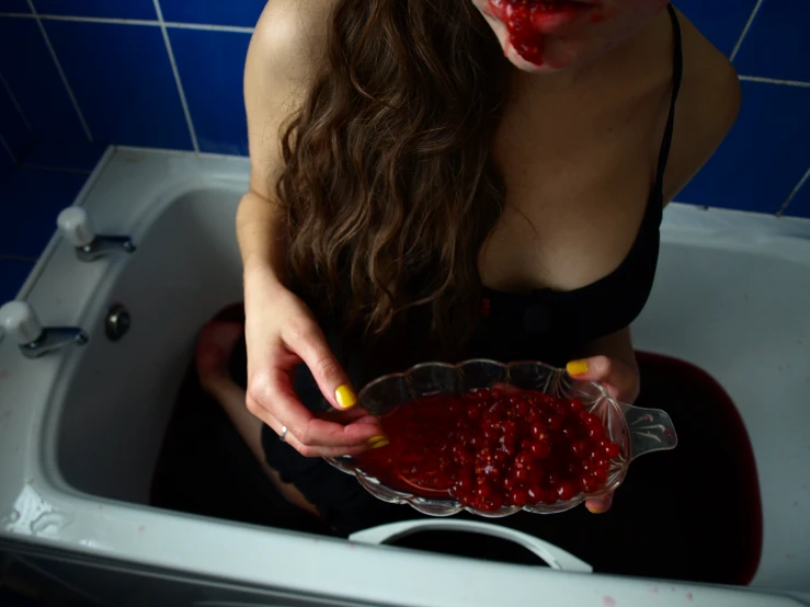 a woman sitting in a bathtub holding a bowl full of red fruit