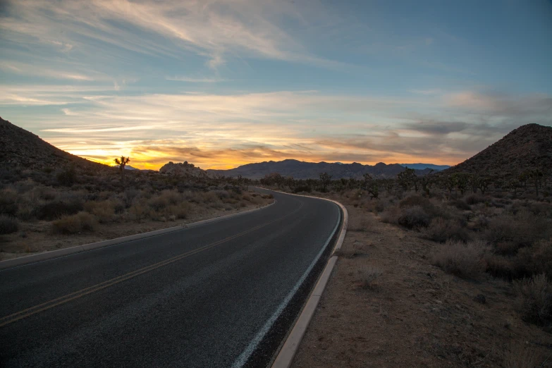 the sun sets over mountains and a winding road