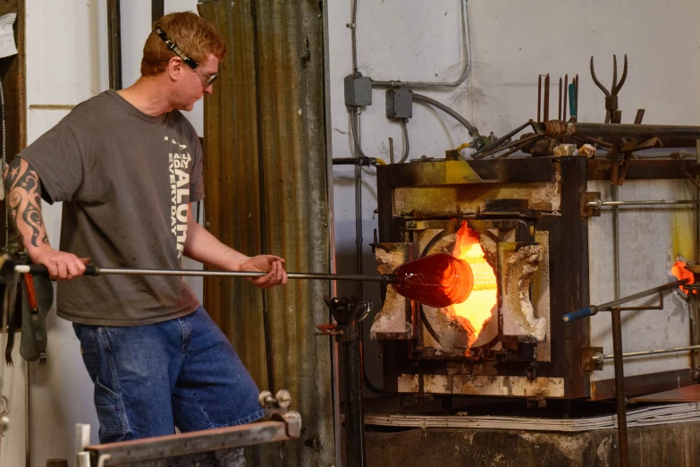 the man is using the blacksmith to make soing with a hammer