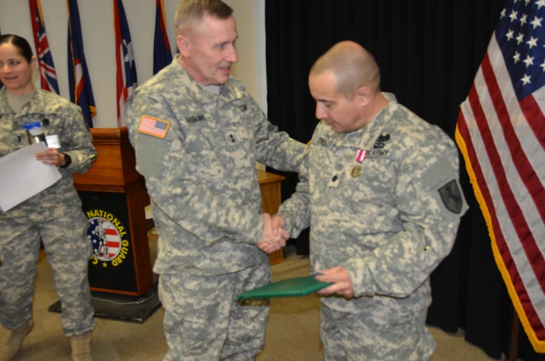 two soldiers shake hands in front of american flags