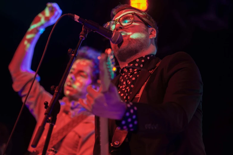 a man singing into a microphone while a woman sings on a stage behind him