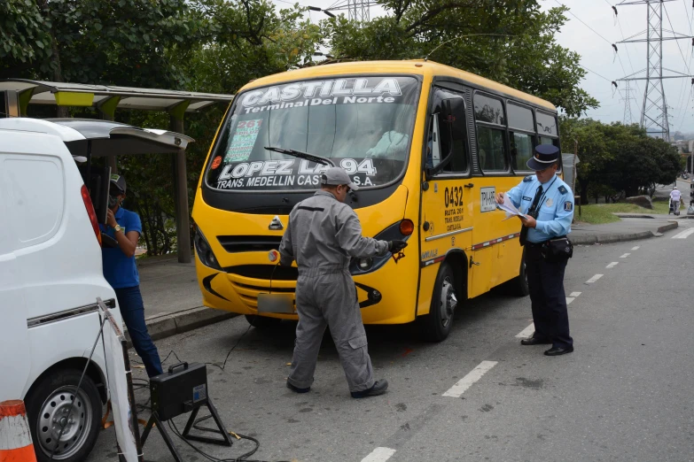 three people are standing near the yellow passenger bus