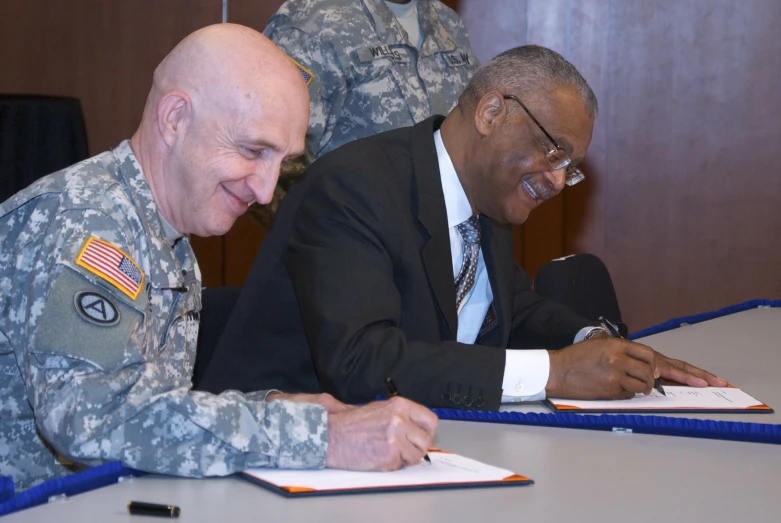 two army soldiers sign documents at a table