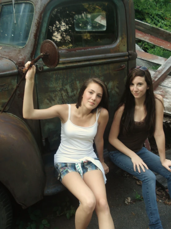 two beautiful young women sitting next to an old truck
