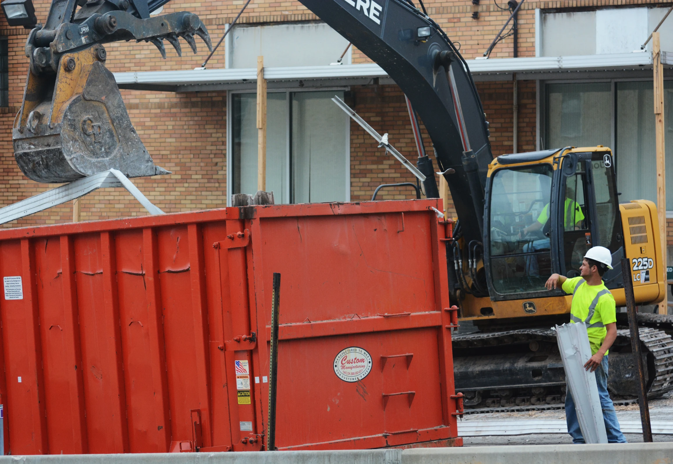 construction workers are next to a dumpster and an excavator