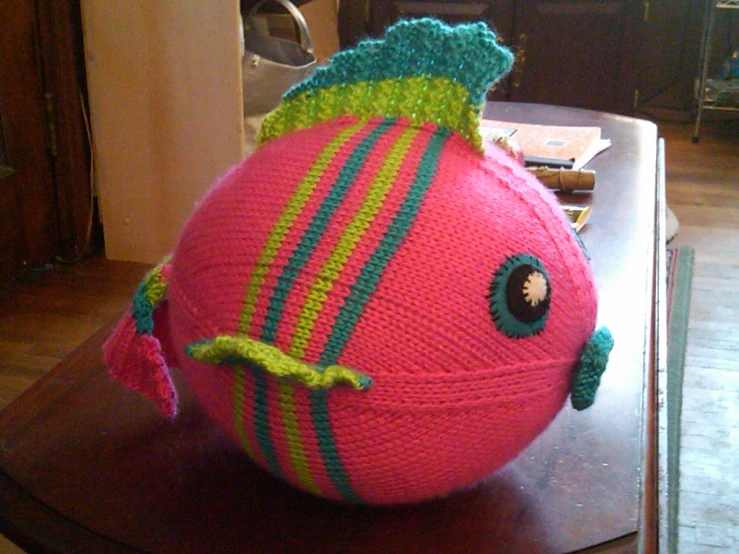 a knitted toy fish on a table next to a cat