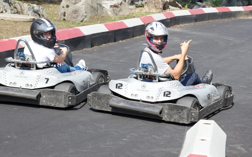 two boys are riding in a go - kart with helmet and gloves on