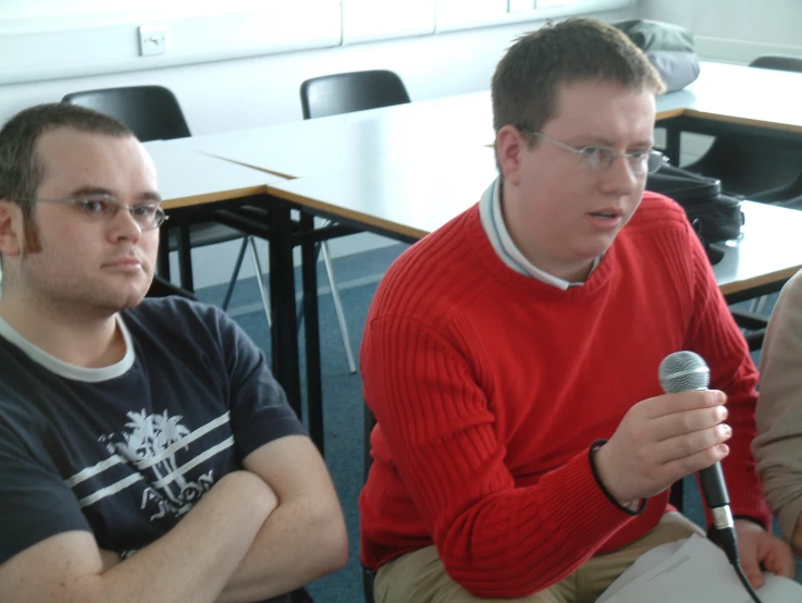 a man sitting at a desk with another person speaking on his phone