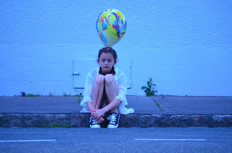 a young woman sitting on a curb next to a wall