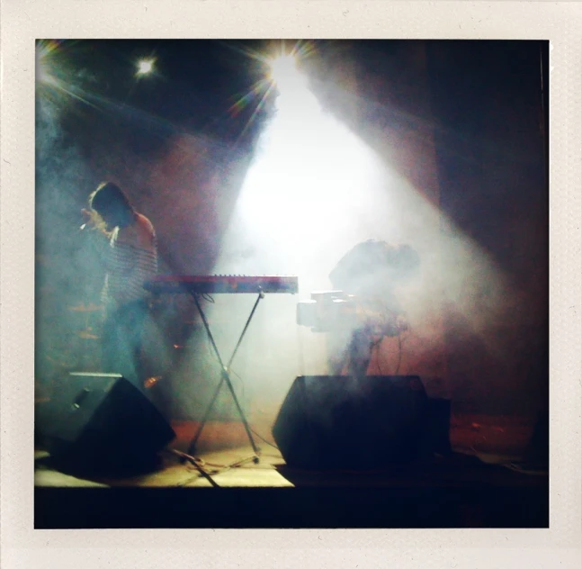 a man stands near an instrument on stage while the light goes from behind him