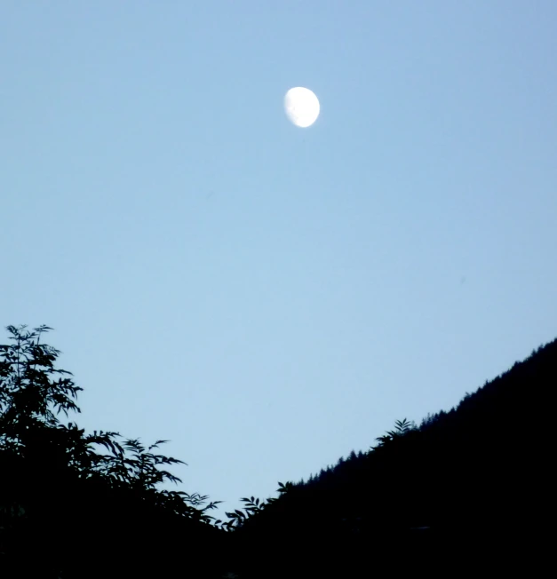 a moon rising over a hill top with trees